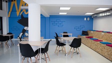 Gemeinschaftsraum mit Tischen und Sesseln mit weiteren Sitzmöglichkeiten sowie kreativer Wandbemalung in blau mit Illustrationen und gelber Schrift