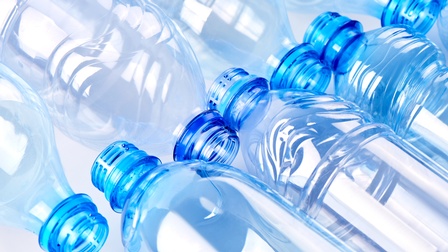 Nahaufnahme von blauen Plastikflaschen, die auf hellem Hintergrund nebeneinander liegen.