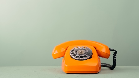 Oranger analoger Telefonapparat mit Wählscheibe vor mintgrünem Hintergrund