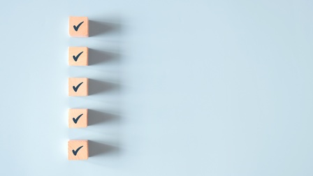 Fünf Holzwürfel mit Häkchen auf hellblauem Hintergrund