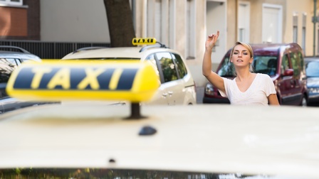 Person mit blonden geschlossenen Haaren hebt die Hand und ruft ein Taxi