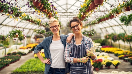Zwei Personen mit Brillen stehen freudig in einem Gewächshaus voller Pflanzen beisammen 
