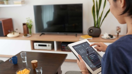Eine Person mit einem Tablet in der Hand bedient die Steuerung einer Smart-Home Anlage