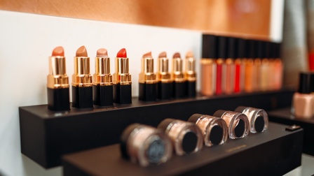 Fokus auf verschiedene Lippenstifte, die aneinandergereiht bei Produktaufsteller präsentiert werden, daneben sind weitere Beauty-Produkte gelistet