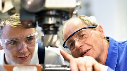 Zwei Personen mit Schutzbrillen inspizieren CNC-Maschine