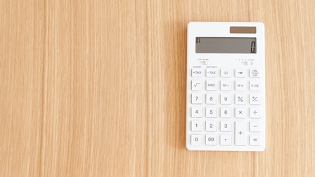 Ein weißer Taschenrechner in rechter Bildhälfte auf Holzuntergrund