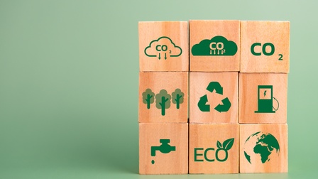 Neun Würfel in drei Reihen mit jeweils drei Würfeln. Die obere Reihe zeigt jeweils den Begriff CO2. In der Mitte sind Bäume, das Recyclingzeichen und eine Ladestation mit Blitzsymbol. Unten sind ein Wasserhahn, der Schriftzug „ECO“ und eine Weltkugel
