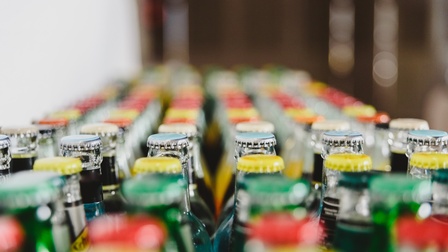 Nahaufnahme von vielen hinter- und nebeneinander stehender mit Kronkorken verschlossener Glasflaschen.