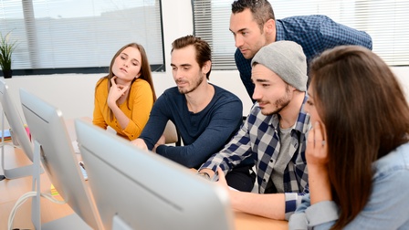 Personen sitzt in einem Raum vor mehreren Computerbildschirmen und blicken darauf