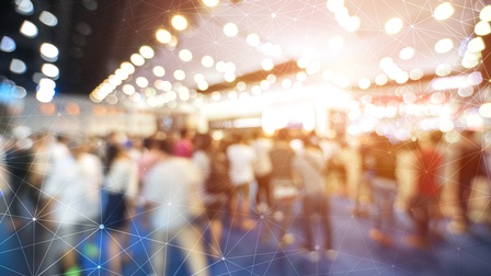 Verschwommene Aufnahme mehrerer Personen in einem Raum, die stehen oder sich bewegen. Darüber liegt eine Grafik, bestehend aus feinen, weißen Strichen, die kreuz und quer über das Bild verlaufen und miteinander verbunden sind