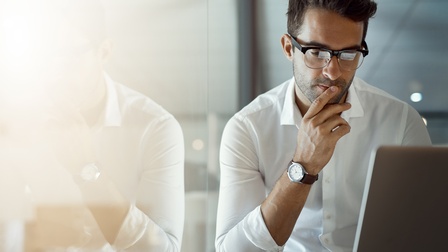 Mann in weißem Hemd sitzt vor Laptop