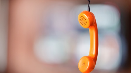 Oranger Telefonhörer kopfüber an schwarzem Telefonkabel hängend, Hintergrund verschwommen