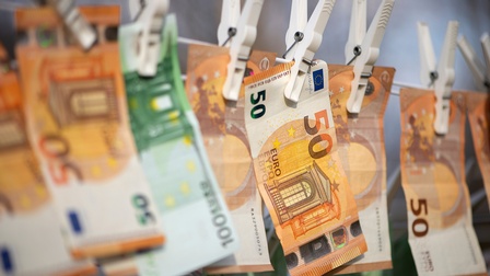 Nahaufnahme einer Wäscheleine, an der viele Geldscheine mit Wäscheklammern befestigt sind. Auf manchen Geldscheinen steht 100, auf anderen 50.