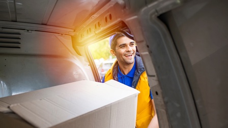 Lächelnde Person mit gelber Weste hebt Paket aus Transporterinnerem
