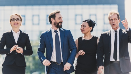 Vier Personen in Businesskleidung nebeneinander schreitend