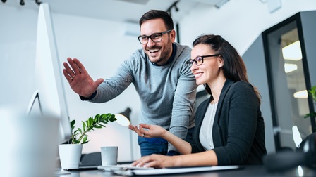 Personen mit Brillen blicken freudig auf einen Bildschirmmonitor in einem hellen, modernen Büro 