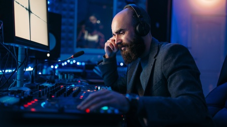 Person mit Bart und Kopfhörern bedient Mischpult