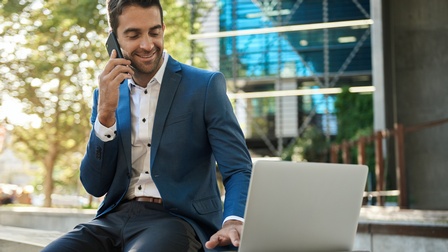 Mann sitzt in Anzug telefonierend vor Laptop