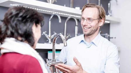 Ein Installateur mit einem Wasserhahn in der Hand bei der Kundeberatung