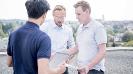 Drei Personen stehen um einen Installationsplan zusammen