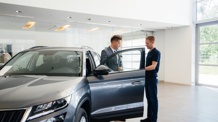 Zwei Personen bei Auto mit geöffneter Fahrertüre stehend
