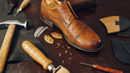 Lederschuh in Herstellungsstatus, ringsum Werkzeuge und Utensilien zur Fertigung eines Schuhs