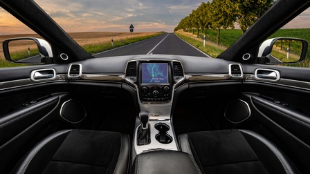 Ein leeres, autonomes Auto fährt mithilfe der Navigation auf einer Landstraße bei Sonnenuntergang. Links und rechts befinden sich Bäume und Grünflächen.