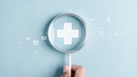 Auf einem hellblauen Hintergrund ist in der Mitte ein weißes Kreuz, auf das eine Hand eine Vergrößerungslupe hält. Links und rechts davon sind weitere, verschiedene, weiße Symbole, wie ein Herz, eine Tablette, ein Tropfen, ein Monitor, ein Bett, eine Uhr