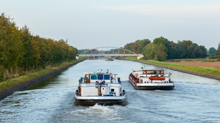 Zwei Schiffe auf Fluss fahrend, ringsum grüne Landschaft und Brücke