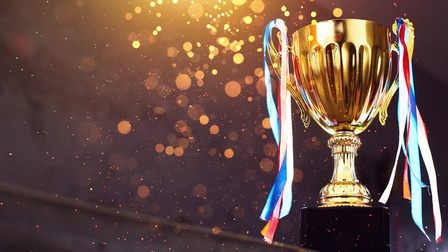 Goldener Pokal mit bunten Fädchen vor einem dunklen Hintergrund mit goldenem Bokeh, Konzept Sieg