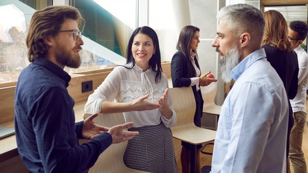 Personen in Businesskleidung stehen gemeinsam in einem modernen Büroraum und unterhalten sich