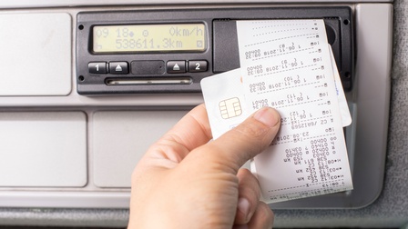 Digitaler Fahrtenschreiber und eine Hand, die einen Ausdruck mit einer Fahrerkarte hält