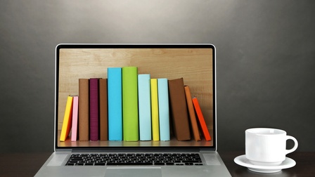 Aufgeklapptes Notebook auf dessen Display nebeneinander stehende Bücher zu sehen sind, nebenstehend eine weiße Tasse auf Unterteller