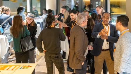 Menschen bei einer Veranstaltung, die sich unterhalten. Sie stehen an runden Tischen. 