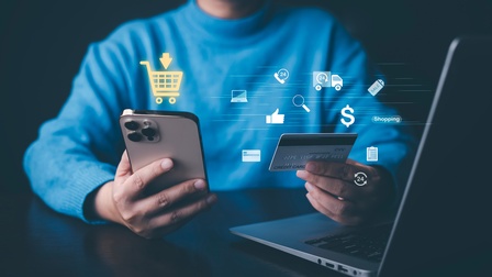 Eine Person hält ein Smartphone in der Hand und bkauft mit einer Kreditkarte online ein