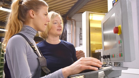 Zwei Personen stehen vor Monitor einer Anlagenregelung, eine Person hält Steuerungsmaus in Hand