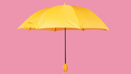 Gelber aufgespannter Schirm auf rosa Hintergrund