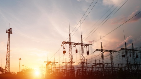 Viele Starkstrommasten unter bewölktem Himmel im Sonnenuntergang.