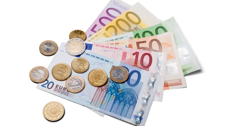 Detailansicht von 10-, 20-, 50-, 100-, 200- und 500-Euro-Geldscheinen in einem Fächer angeordnet, auf denen verschiedene Euromünzen liegen.