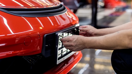 Hände befestigen ein Nummernschild an einem roten Auto