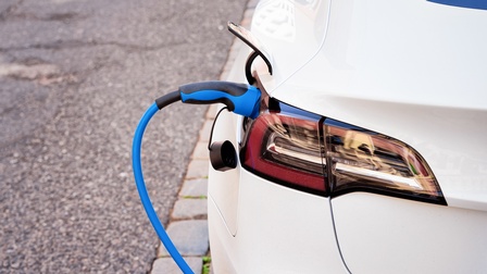 Ausschnitt eines weißen Elektroautos in Rückansicht mit Fokus auf Stromladetank, in dem blauer Charger steckt