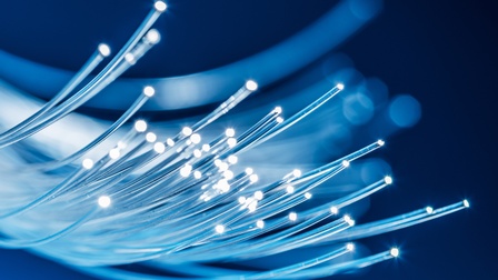 Nahaufnahme von vielen langen, dünnen, runden Kabeln, deren Enden hell leuchten, auf dunklem Untergrund