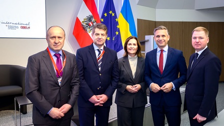Porträt von fünf Personen in dunklen Anzügen, die in einem Raum nebeneinander vor einer österreichischen, einer ukrainischen und einer Flagge der europäischen Union stehen und lächeln