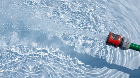 Von rechter Seite ein Schlauch aus dem Wasser fließt und einen Pool befüllt