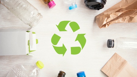 Eine grafische Darstellung eines grünen Recycling-Symbols: Drei Pfeile im Kreis laufend. Drumherum liegen unterschiedliche recycelbare Verpackungen wie Flaschen, Tüten und Becher.