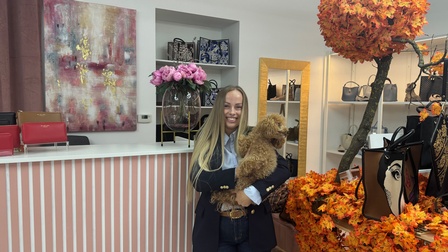 Porträt einer Person in einem Sakko und langen, offenen, hellen Haaren, die in einem Geschäft steht und einen Hund hält