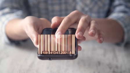 Eine Hand hält einen Laserscanner vor dem ein Strichcode abgebildet ist