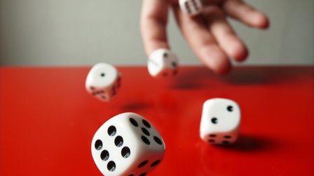 Nahaufnahme der rechten Hand einer Person, die mit fünf Würfeln würfelt