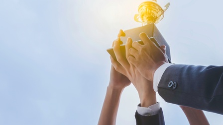 Vier Personen halten gemeinsam einen Pokal in die Höhe