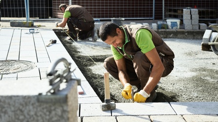 Zwei Männer pflastern einen Straße mit Steinen. Zuerst spannen sie eine Schnur zur Orientierung